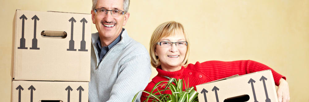 A senior couple smiling while holding moving boxes